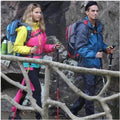 A woman and a man outdoors trekking, both holding a carbon fiber hiking pole in each of their hands. They are carrying a backpack each.