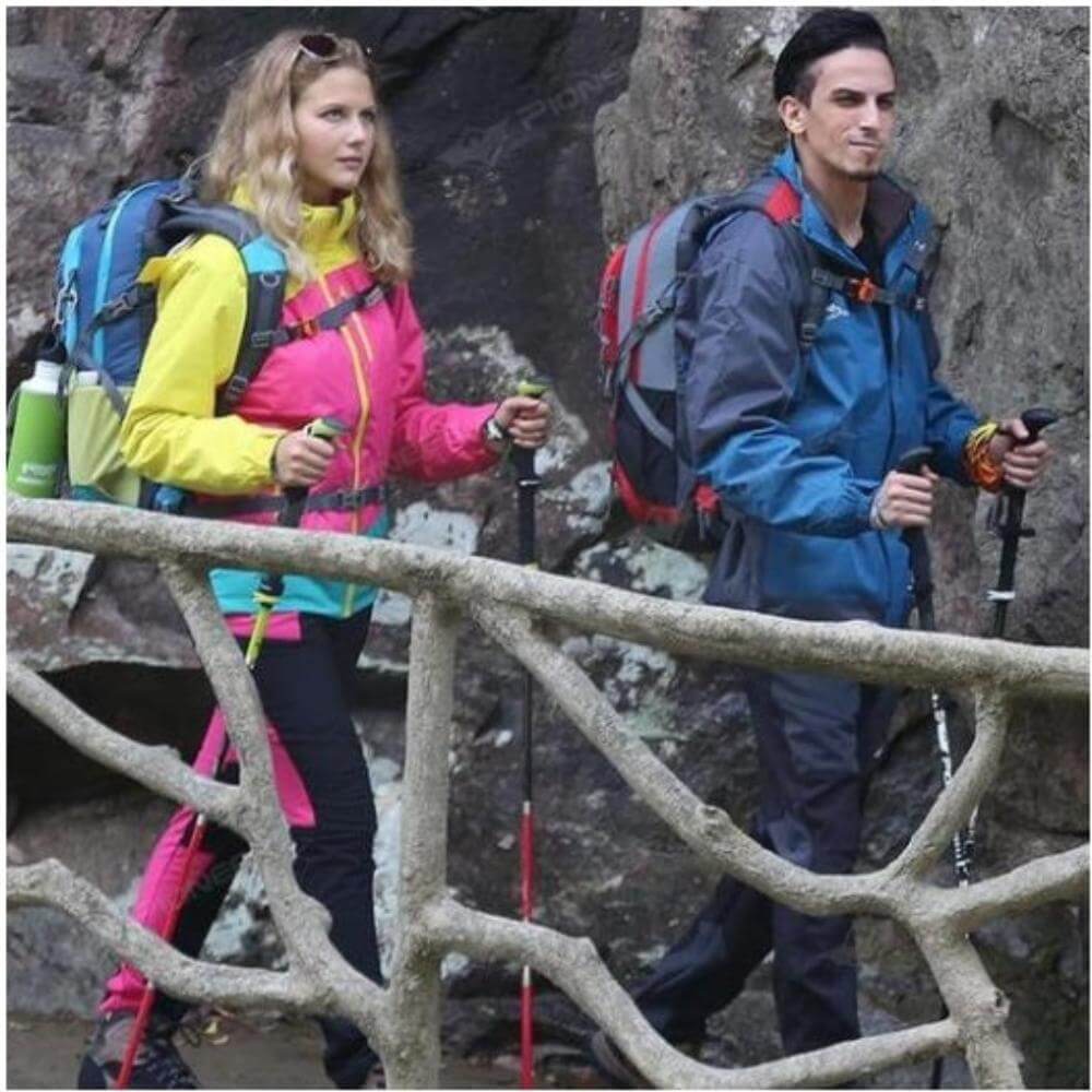 A woman and a man outdoors trekking, both holding a carbon fiber hiking pole in each of their hands. They are carrying a backpack each.