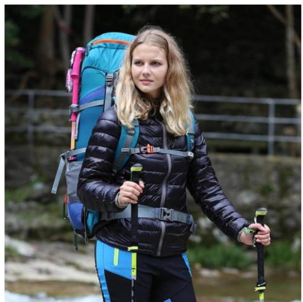 A woman outdoors trekking with a carbon fiber hiking pole in each hand and carrying a big backpack.